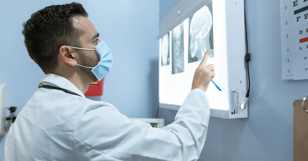 A healthcare professional examines brain X-rays while wearing a face mask in a hospital setting.