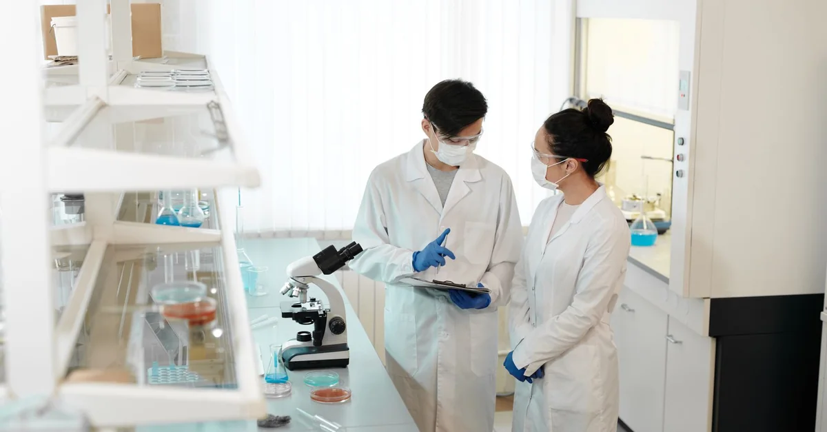 Two scientists discussing research with a microscope in a modern lab.