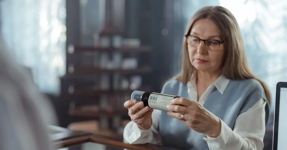 A woman reading the label on a bottle at a pharmacy counter.
