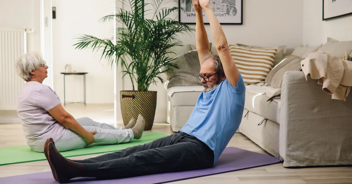 Elderly couple enjoying yoga exercise on mats at home, promoting healthy and positive aging.