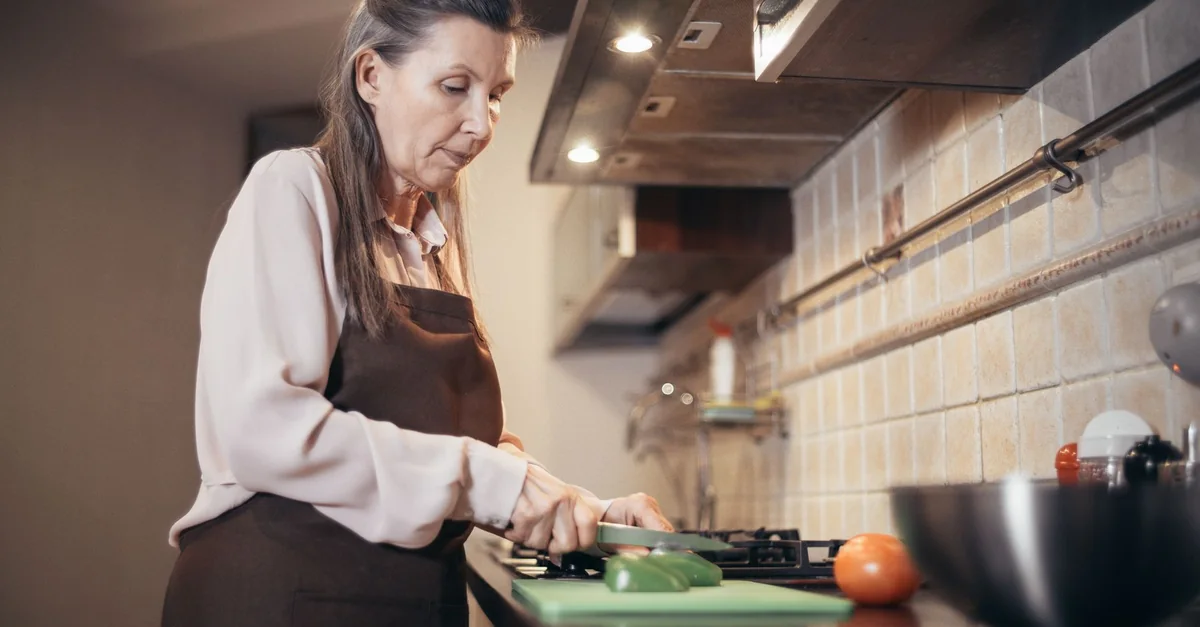 Senior woman chopping vegetables in a warm, cozy kitchen setting. Engaged in daily home cooking.