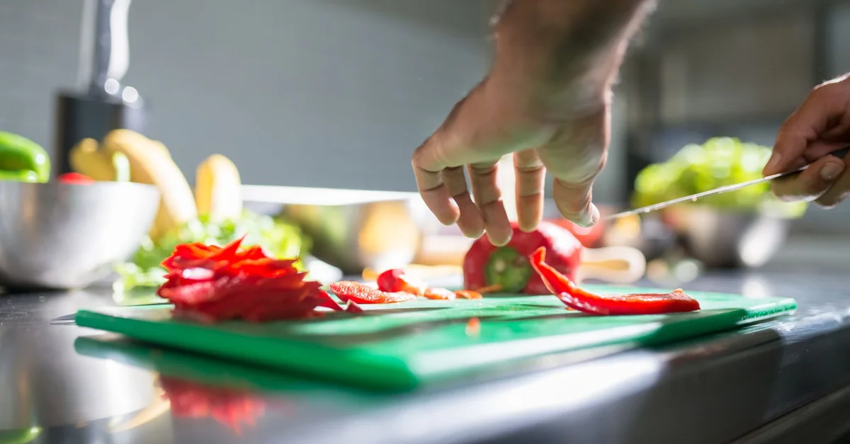 Hands slicing red bell pepper on a chopping board in a kitchen setting, ideal for culinary visuals.