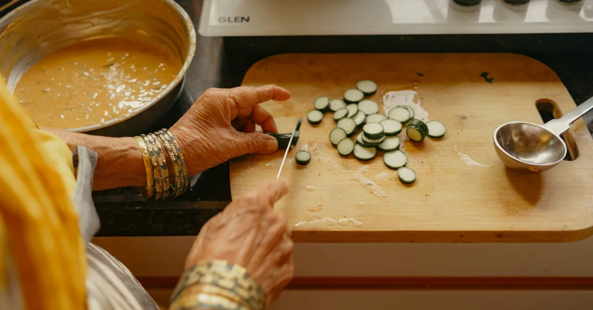 Senior Indian woman chops vegetables in a kitchen, preparing a meal with traditional methods.