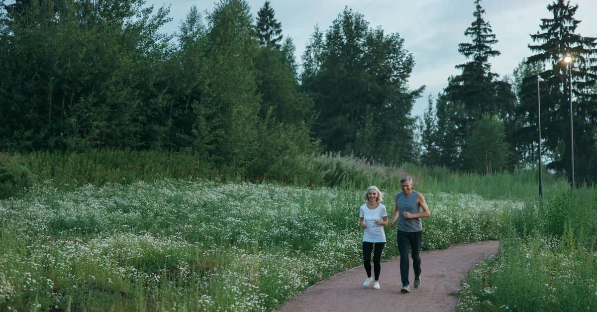 Senior couple jogging on a scenic park path surrounded by greenery.