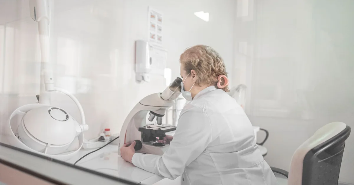 A scientist works with a microscope in a bright, modern lab setting, wearing a lab coat.