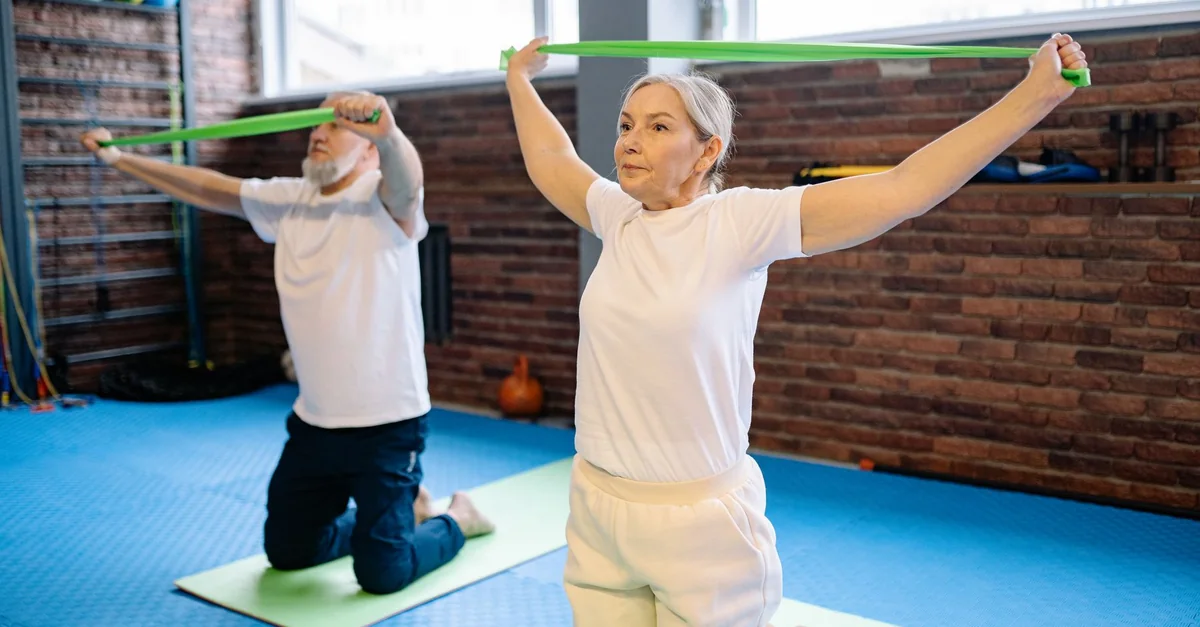 Elderly man and woman performing fitness workout with resistance bands, promoting healthy lifestyle indoors.