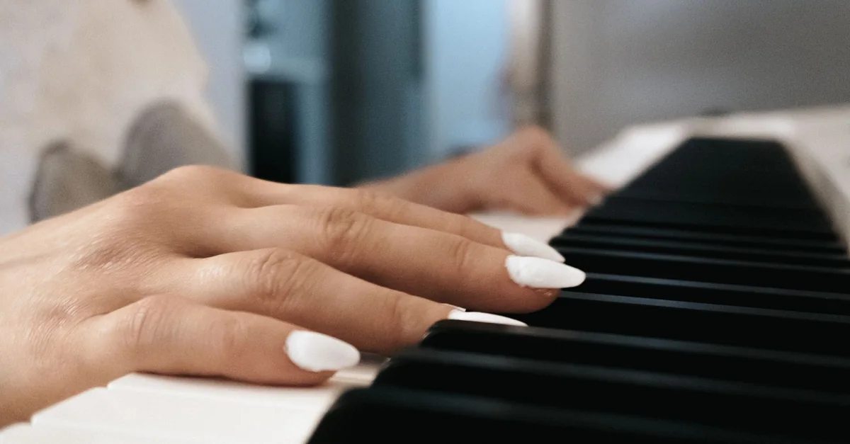 A close-up view of a female adult's hands playing a piano indoors, focusing on fingering technique and white nails.