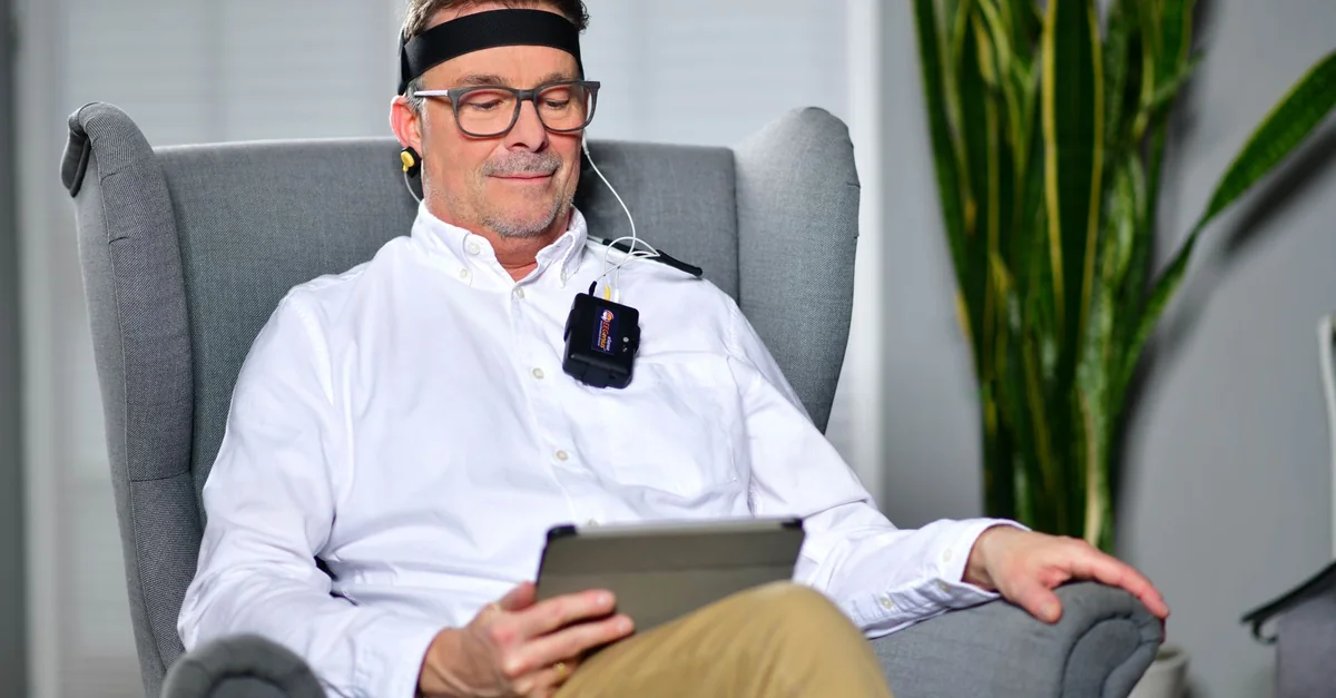 Man sitting in an armchair using a neurofeedback device, illustrating modern technology in healthcare.