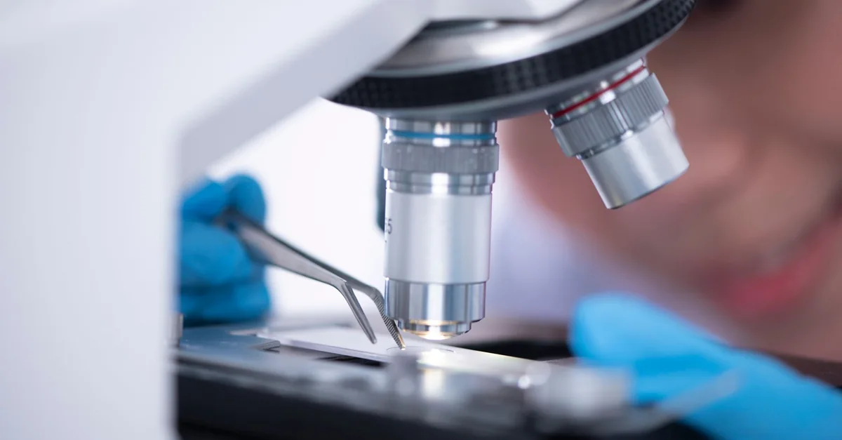 Blurred unrecognizable person placing sample on microscope while making research during work in modern laboratory