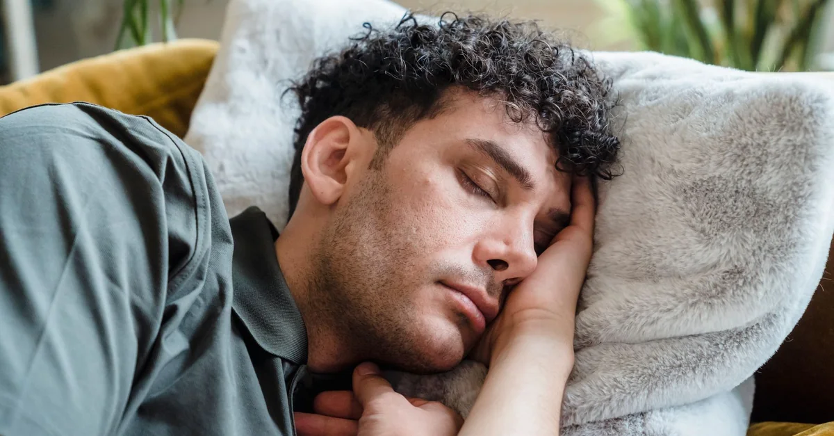A young man with curly hair peacefully sleeping on a cozy couch with a soft pillow.