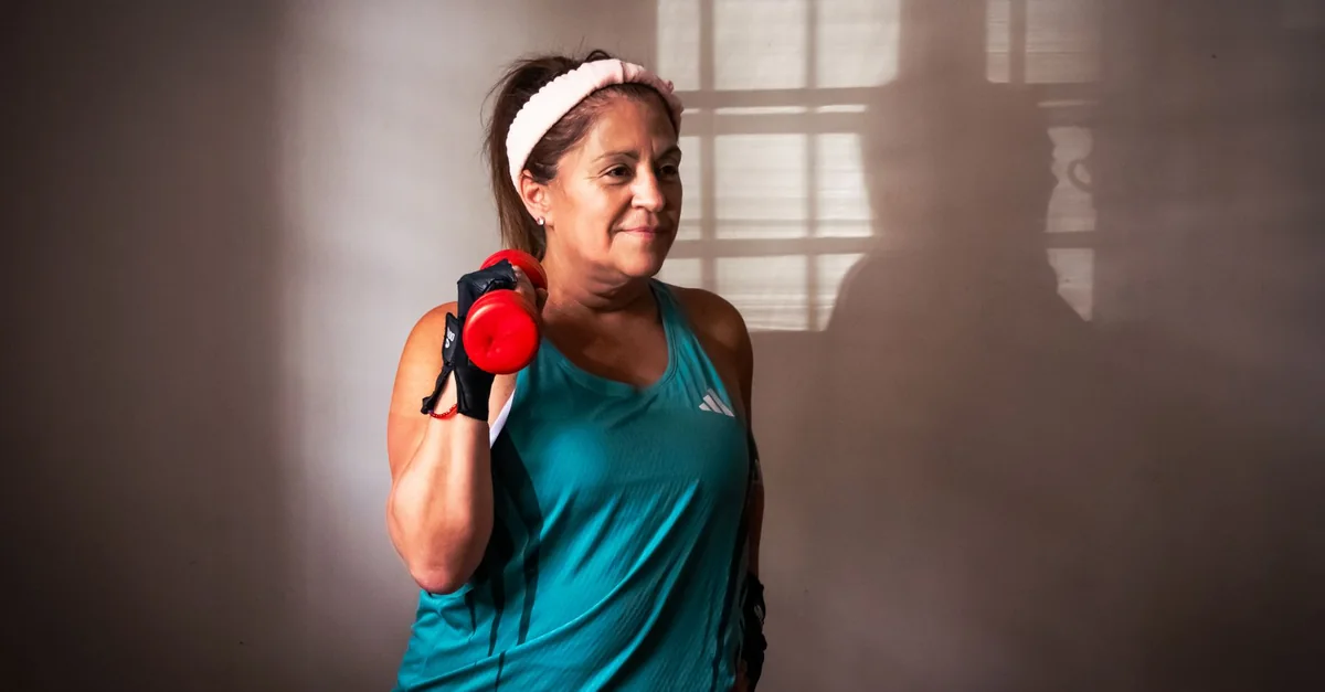 Middle-aged woman in gym attire lifting a dumbbell indoors, showing a fitness and healthy lifestyle theme.
