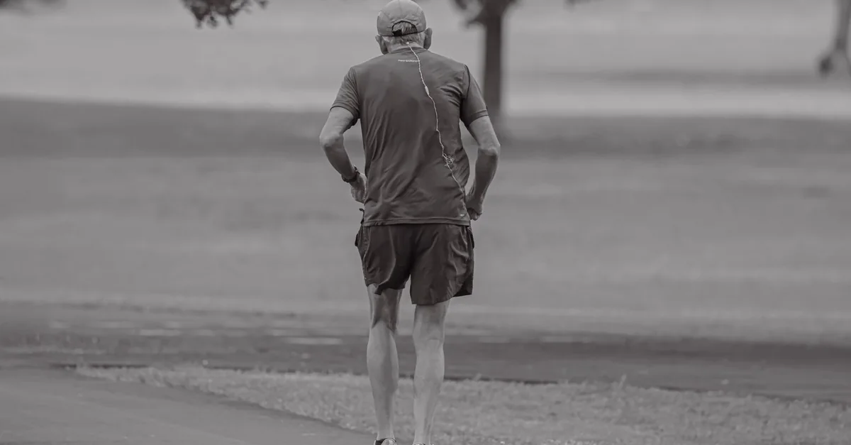 A senior man jogs alone in a serene park in Stamford, Connecticut, captured at dawn.