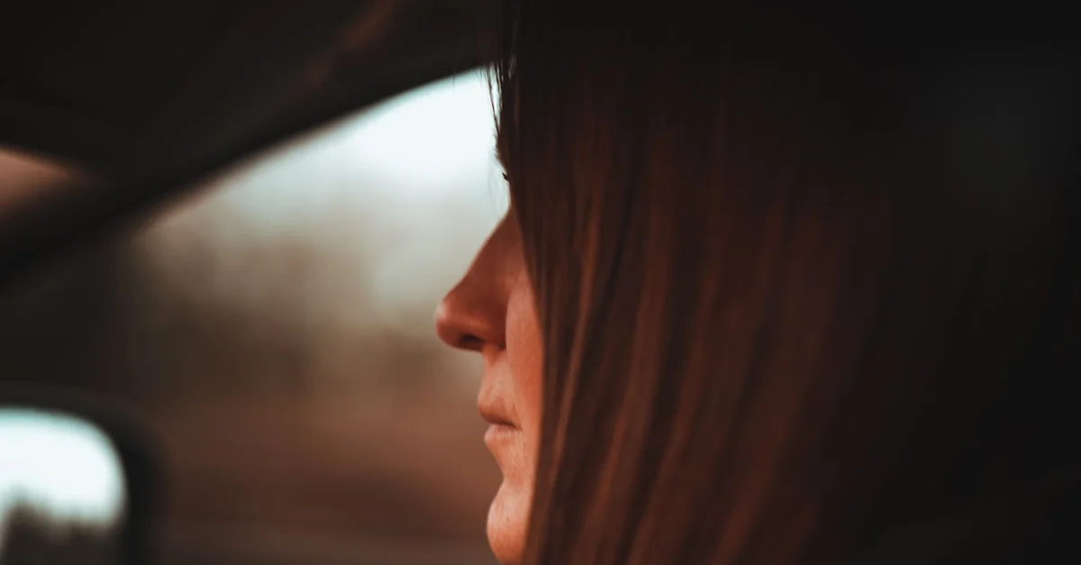 Side profile of a woman driving with a focus on her face in a car interior setting.