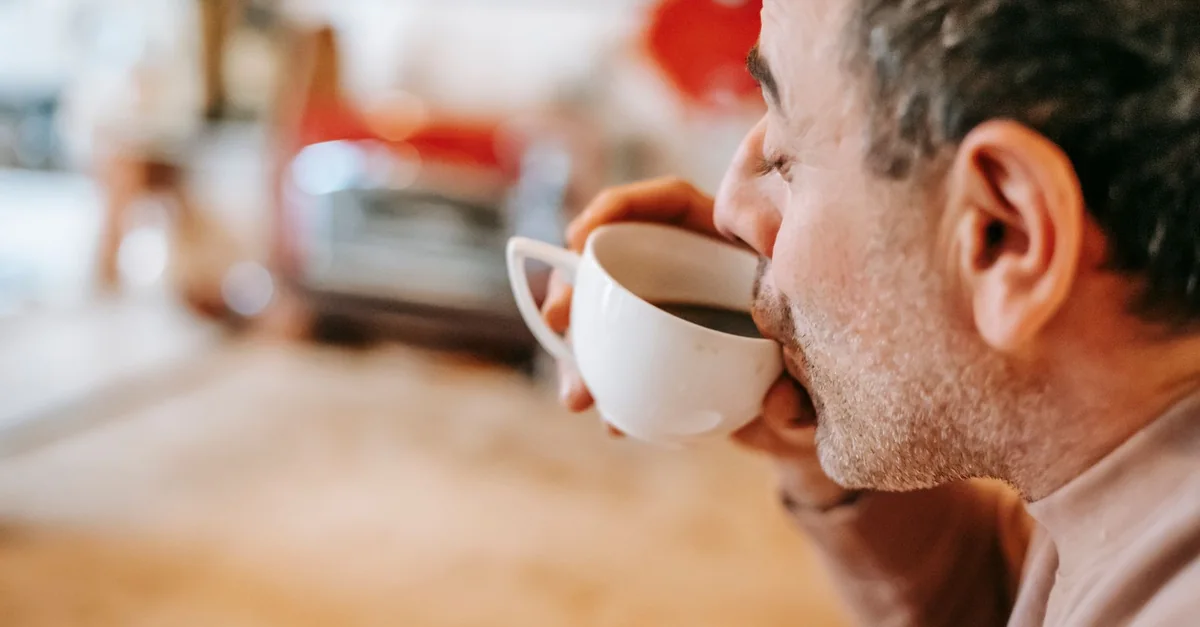 Side view of crop middle aged ethnic male drinking aromatic hot coffee with closed eyes during breakfast at home